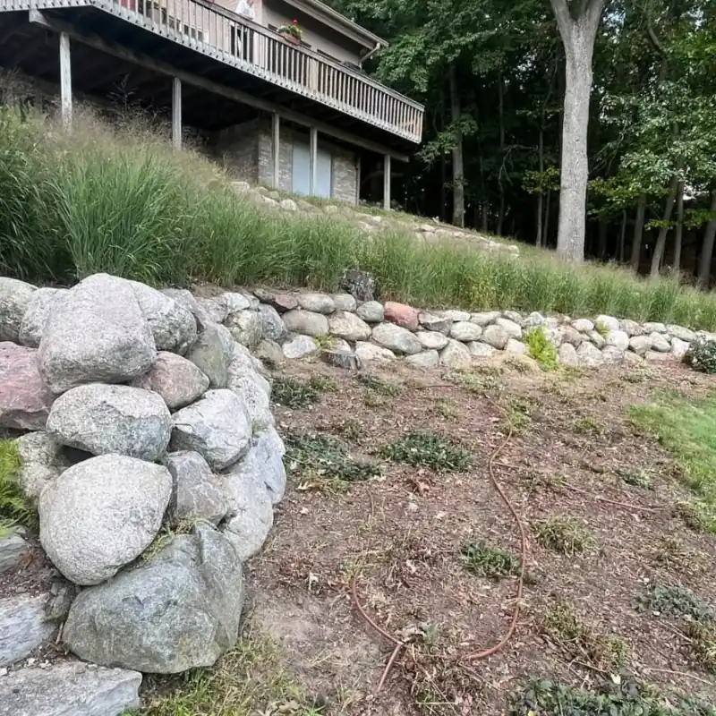 Natural stone retaining wall on a landscaped hillside by Legacy Lawn And Landscape